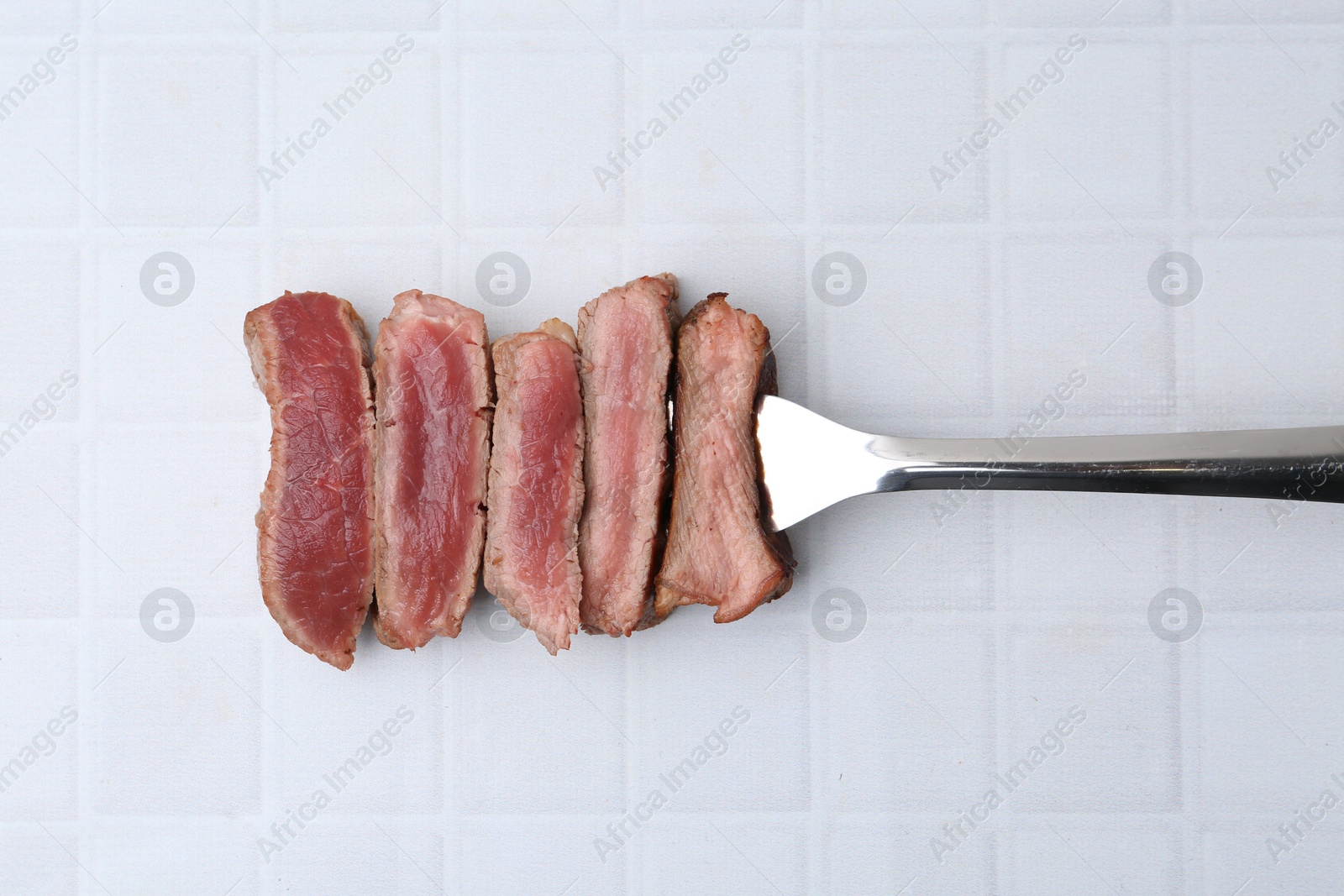 Photo of Delicious sliced beef tenderloin with different degrees of doneness on light tiled table, top view