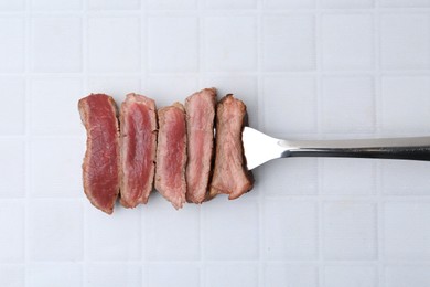 Photo of Delicious sliced beef tenderloin with different degrees of doneness on light tiled table, top view