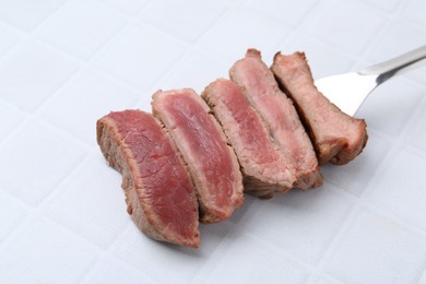 Photo of Delicious sliced beef tenderloin with different degrees of doneness on light tiled table, closeup