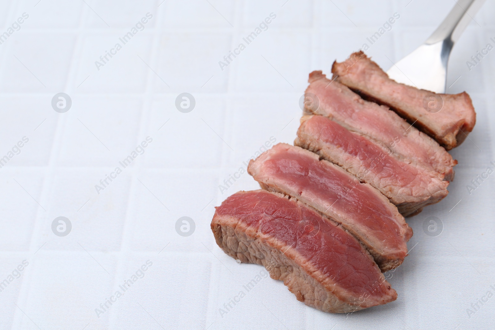 Photo of Delicious sliced beef tenderloin with different degrees of doneness on light tiled table, closeup. Space for text