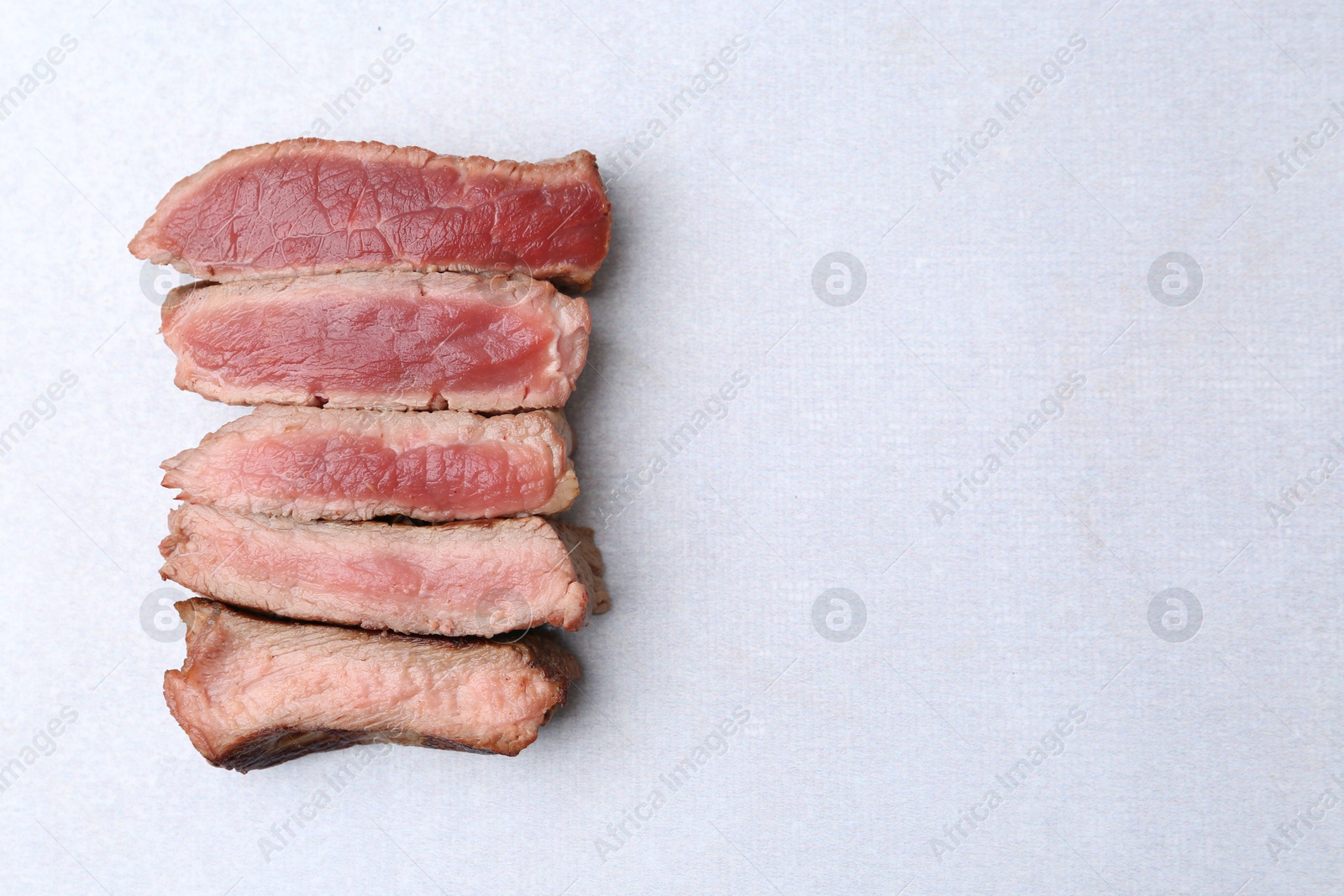 Photo of Delicious sliced beef tenderloin with different degrees of doneness on light table, top view. Space for text