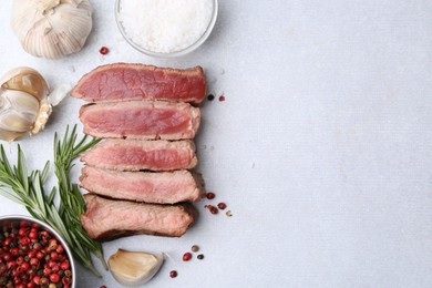 Photo of Delicious sliced beef tenderloin with different degrees of doneness and spices on light table, flat lay. Space for text