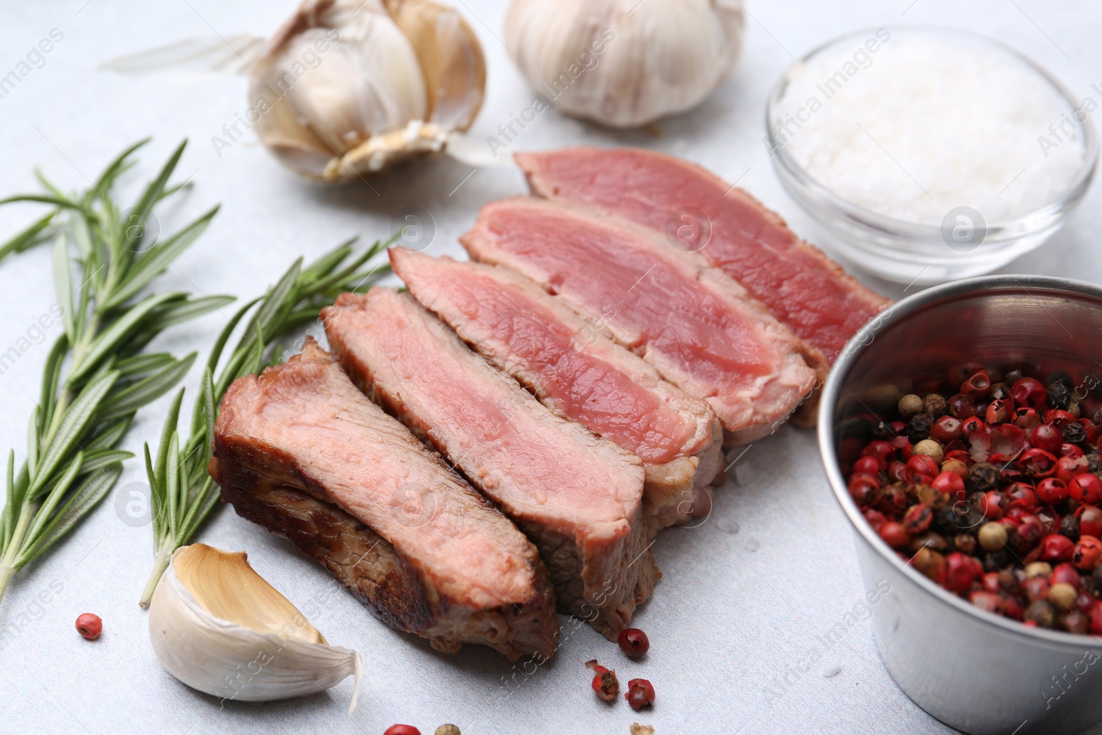 Photo of Delicious sliced beef tenderloin with different degrees of doneness and spices on light table, closeup