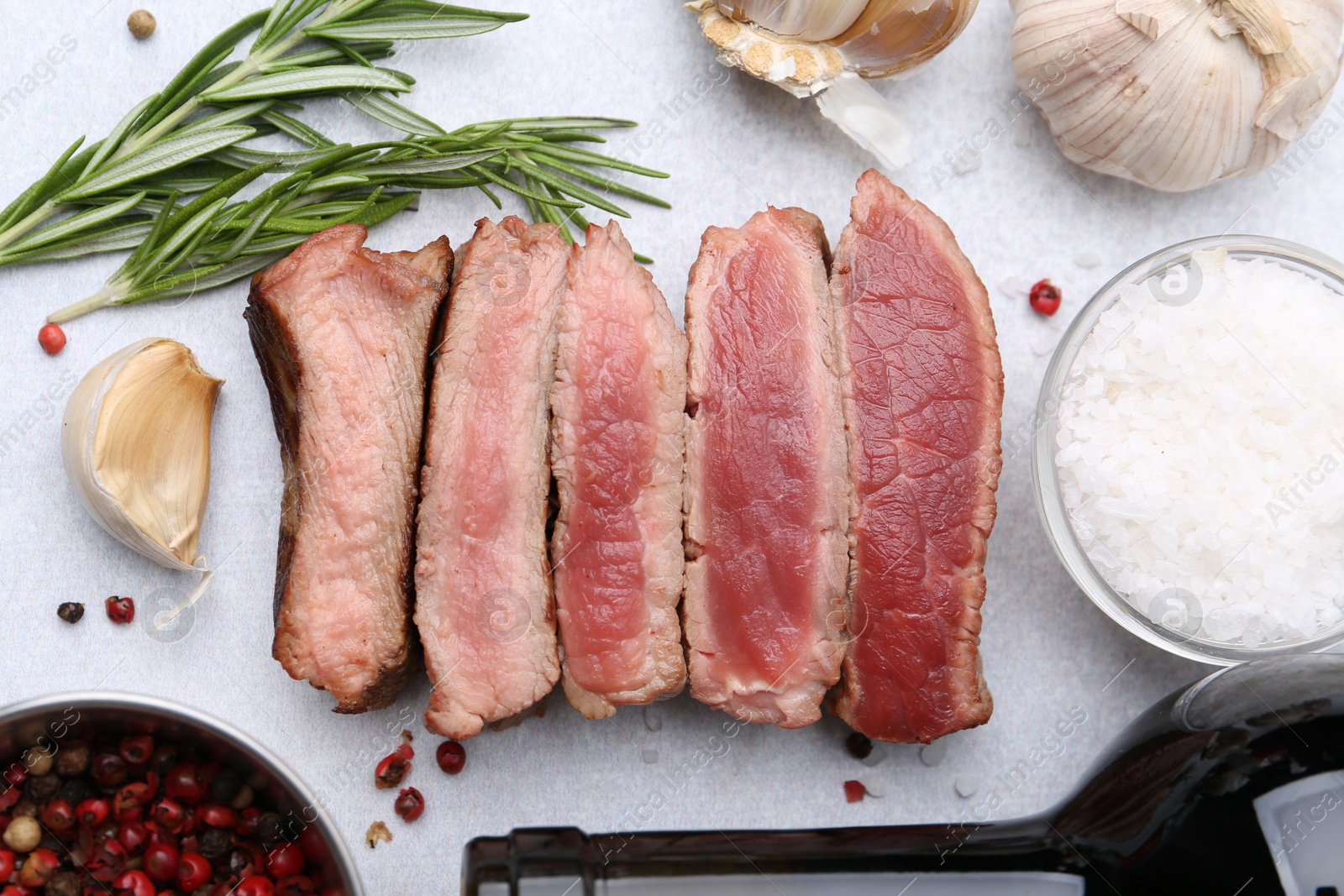 Photo of Delicious sliced beef tenderloin with different degrees of doneness, wine and spices on light table, flat lay