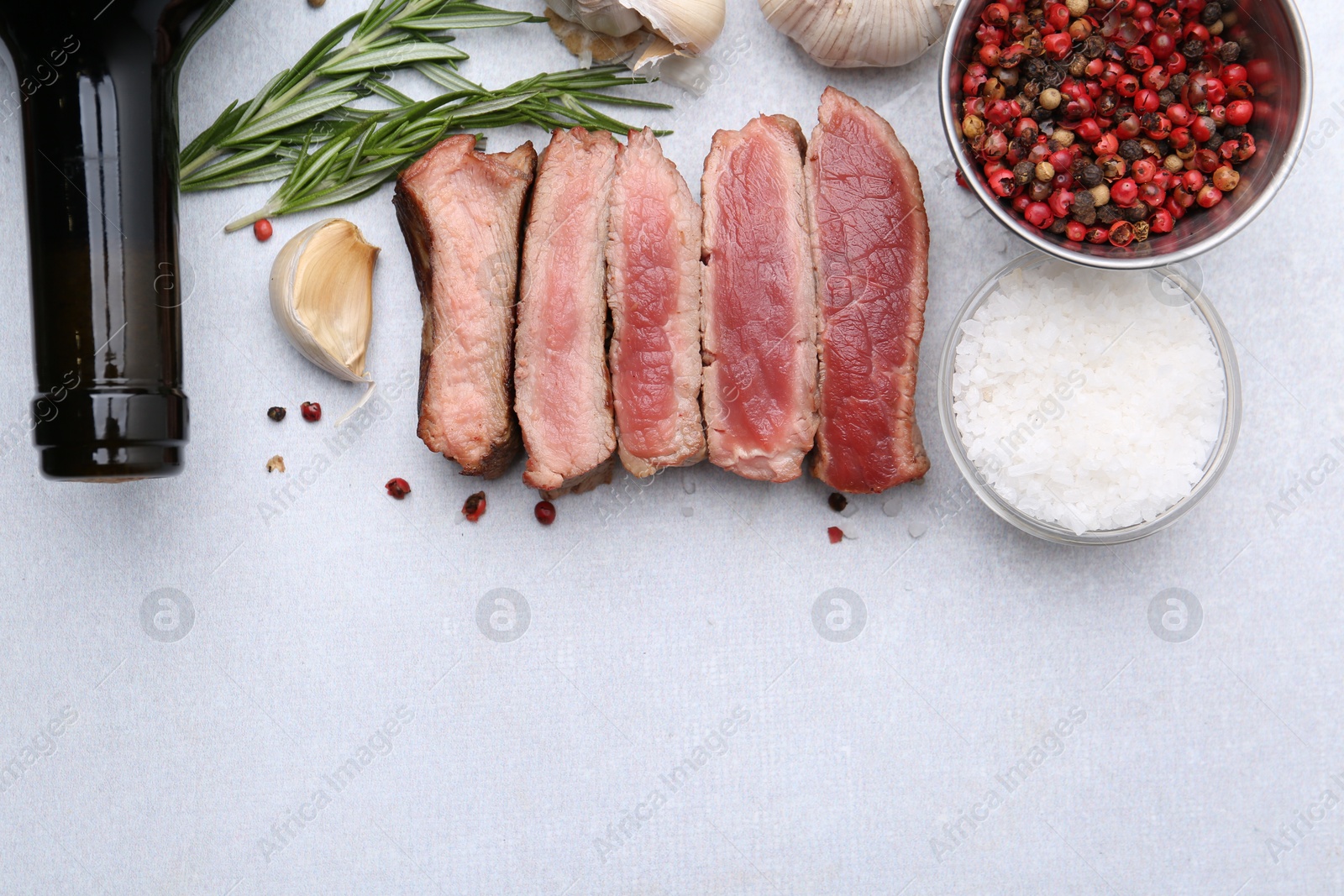 Photo of Delicious sliced beef tenderloin with different degrees of doneness, wine and spices on light table, flat lay. Space for text