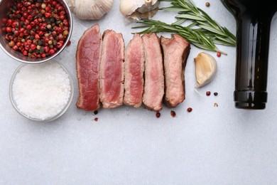 Photo of Delicious sliced beef tenderloin with different degrees of doneness, wine and spices on light table, flat lay