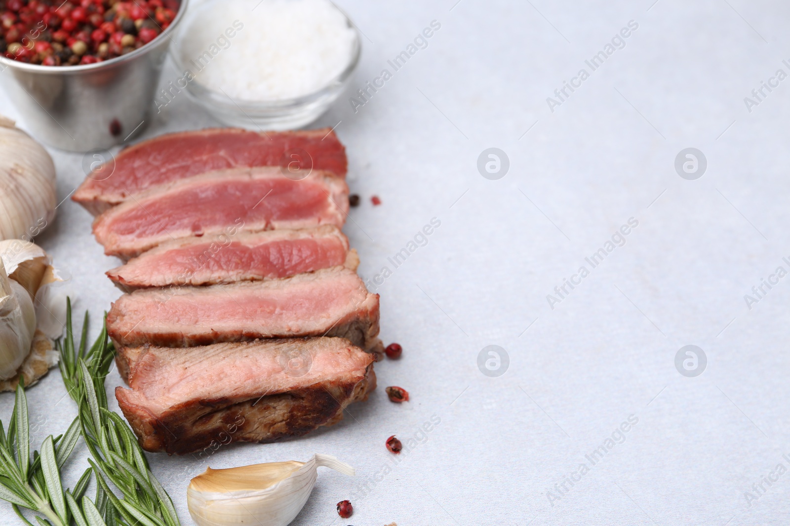 Photo of Delicious sliced beef tenderloin with different degrees of doneness and spices on light table, closeup. Space for text