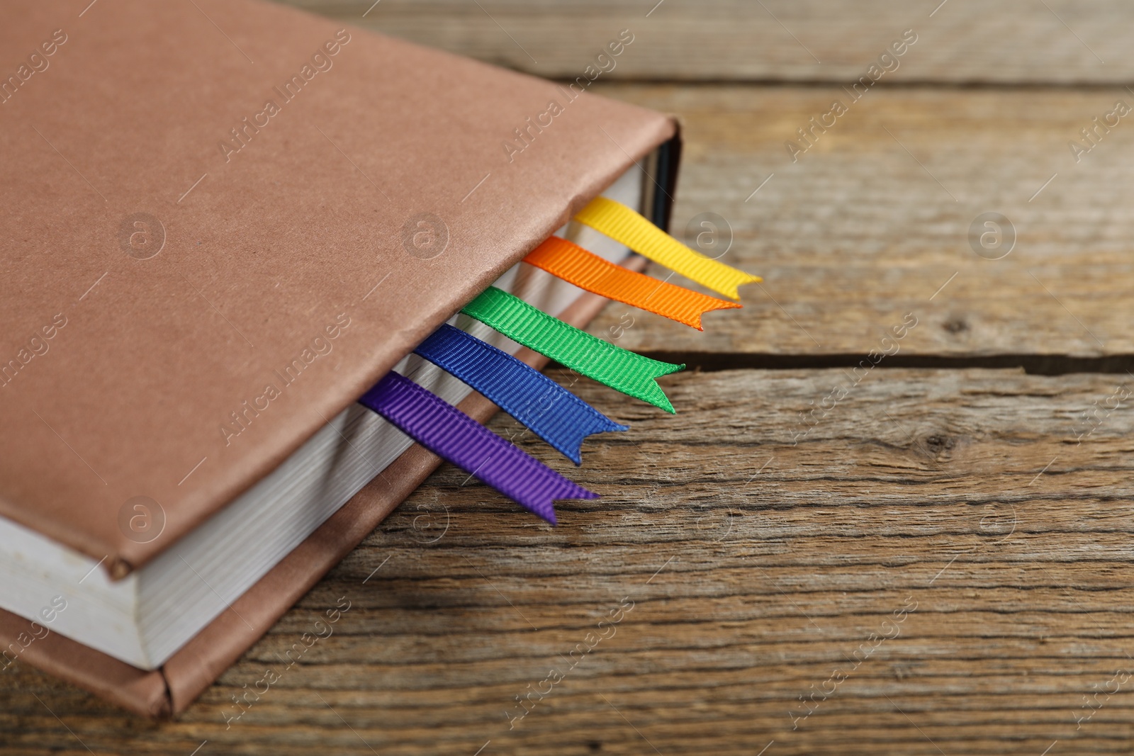 Photo of Book with ribbon bookmarks on wooden table, closeup. Space for text