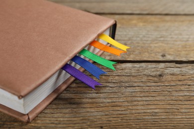 Photo of Book with ribbon bookmarks on wooden table, closeup. Space for text