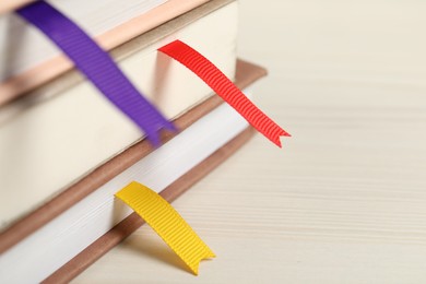 Photo of Books with ribbon bookmarks on light wooden table, closeup. Space for text