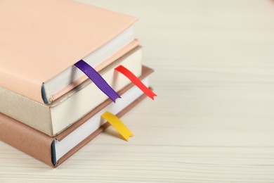 Photo of Books with ribbon bookmarks on light wooden table, closeup. Space for text