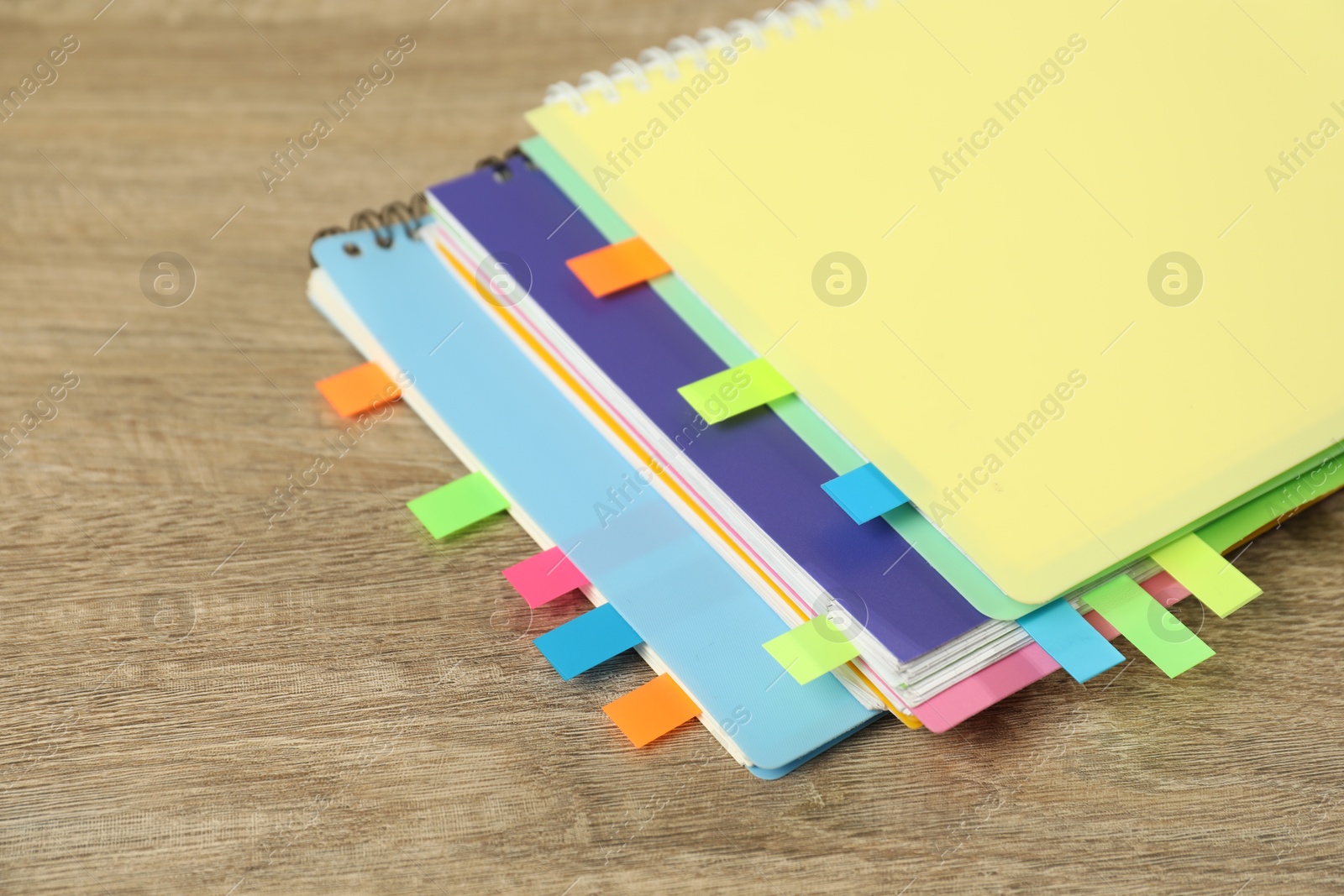 Photo of Notebooks with colorful tabs on wooden table, closeup