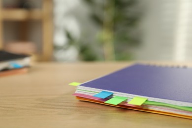 Photo of Notebook with colorful tabs on wooden table indoors, closeup. Space for text