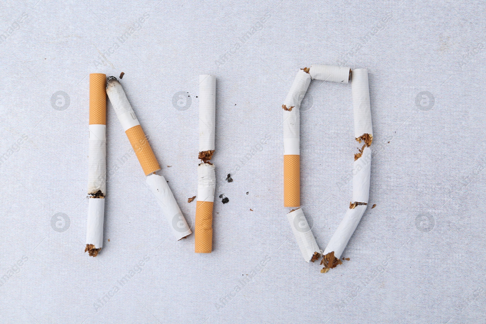 Photo of Word NO made with cigarette butts on light gray background, top view