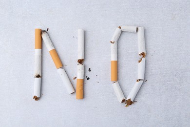 Photo of Word NO made with cigarette butts on light gray background, top view