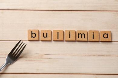 Photo of Word Bulimia and fork on white wooden table, top view