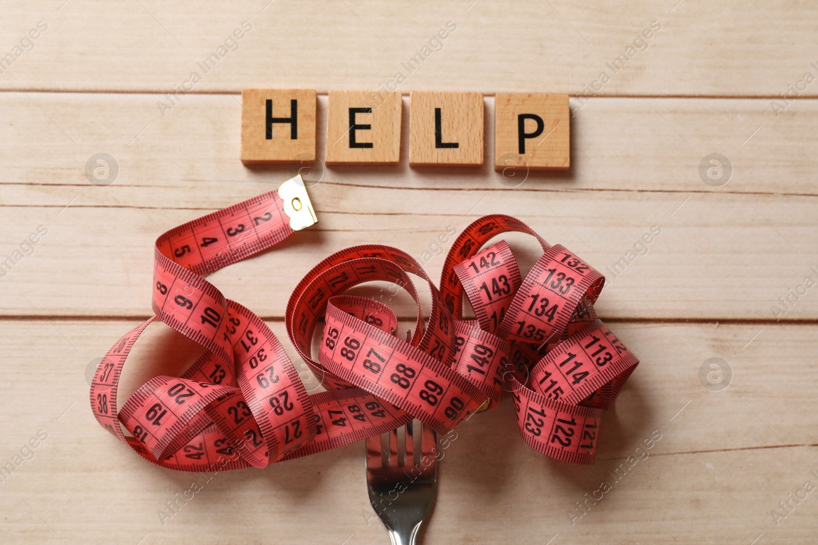 Photo of Bulimia. Word Help and fork with measuring tape on white wooden table, top view