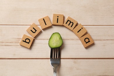 Photo of Word Bulimia and fork with cucumber slice on white wooden table, top view