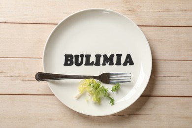 Photo of Plate with word Bulimia, fork and lettuce on white wooden table, top view