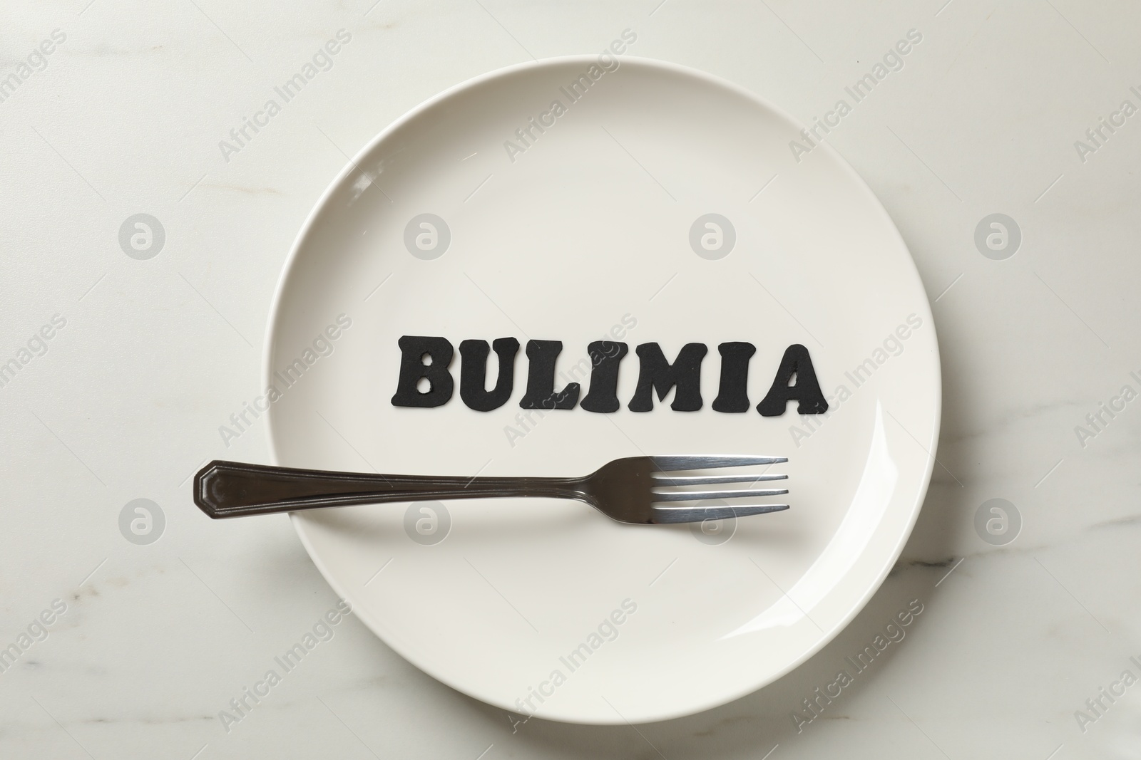 Photo of Plate with word Bulimia and fork on white marble table, top view