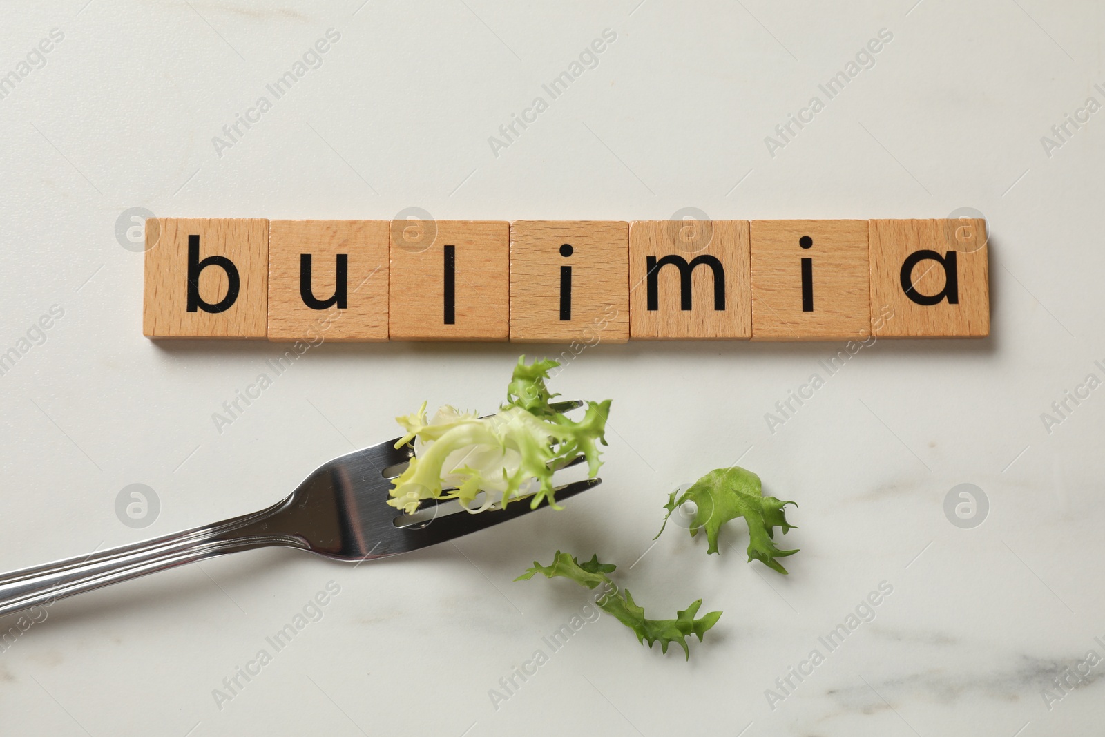 Photo of Word Bulimia and fork with lettuce on white marble table, top view