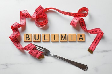 Photo of Word Bulimia, fork and measuring tape on white marble table, top view