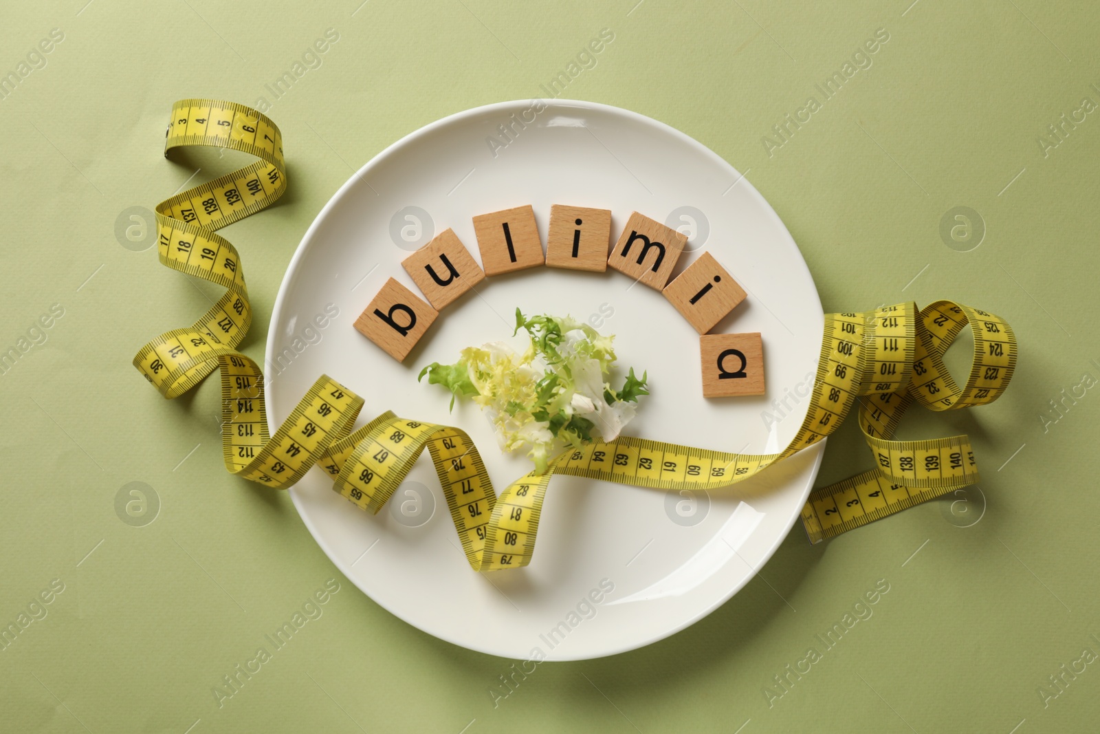 Photo of Plate with word Bulimia, lettuce and measuring tape on olive background, top view