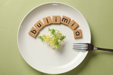 Photo of Plate with word Bulimia, lettuce and fork on olive background, top view