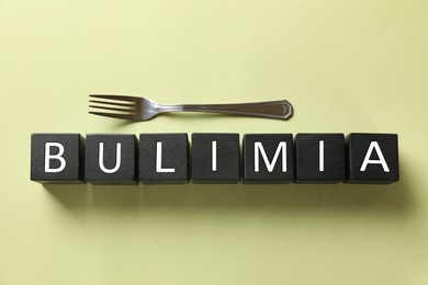 Photo of Word Bulimia and fork on olive background, top view