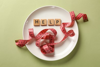 Photo of Bulimia. Plate with word Help and measuring tape on olive background, top view