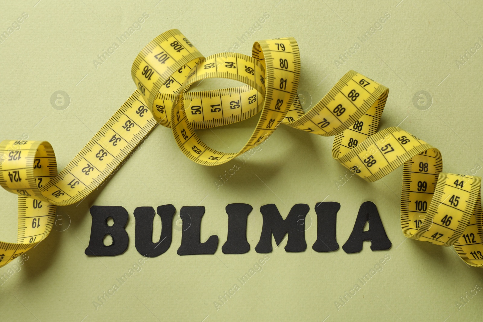 Photo of Word Bulimia and measuring tape on olive background, top view