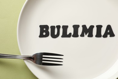 Photo of Plate with word Bulimia and fork on olive background, top view