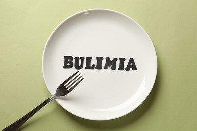 Photo of Plate with word Bulimia and fork on olive background, top view