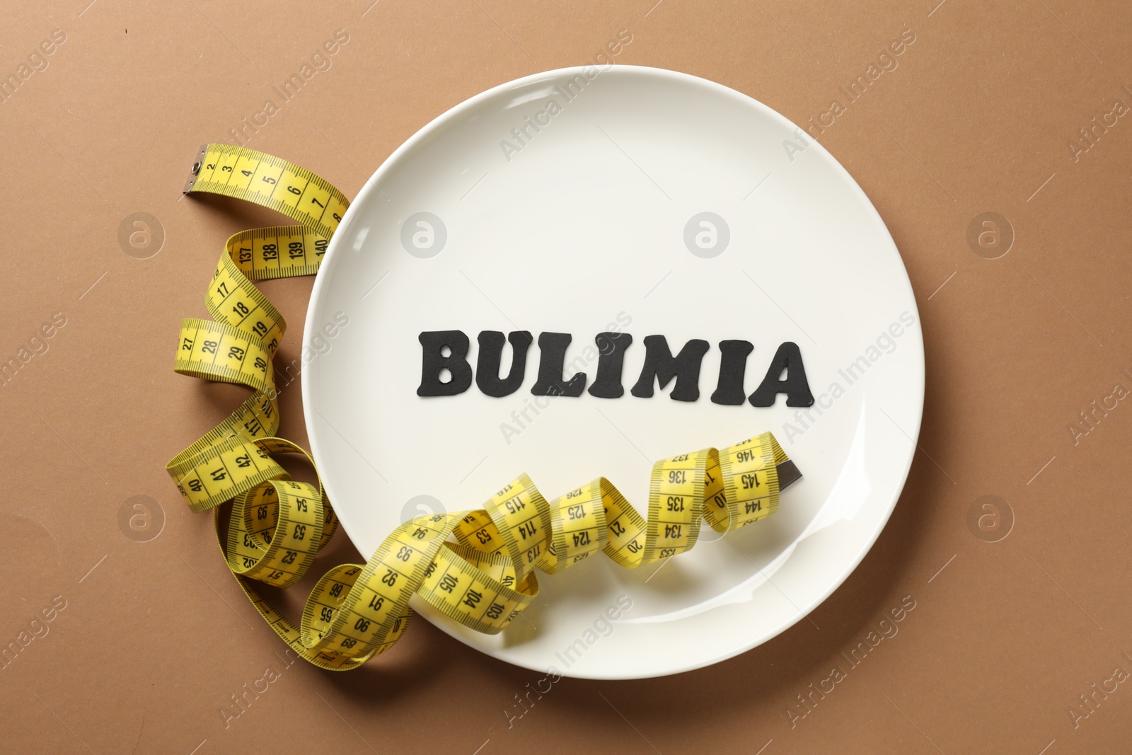 Photo of Plate with word Bulimia and measuring tape on brown background, top view