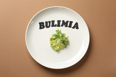 Photo of Plate with word Bulimia and lettuce on brown background, top view