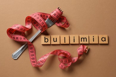 Photo of Word Bulimia, fork and measuring tape on brown background, top view