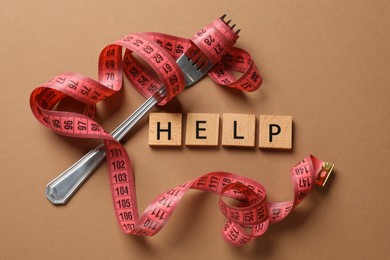 Photo of Bulimia. Word Help, fork and measuring tape on brown background, top view