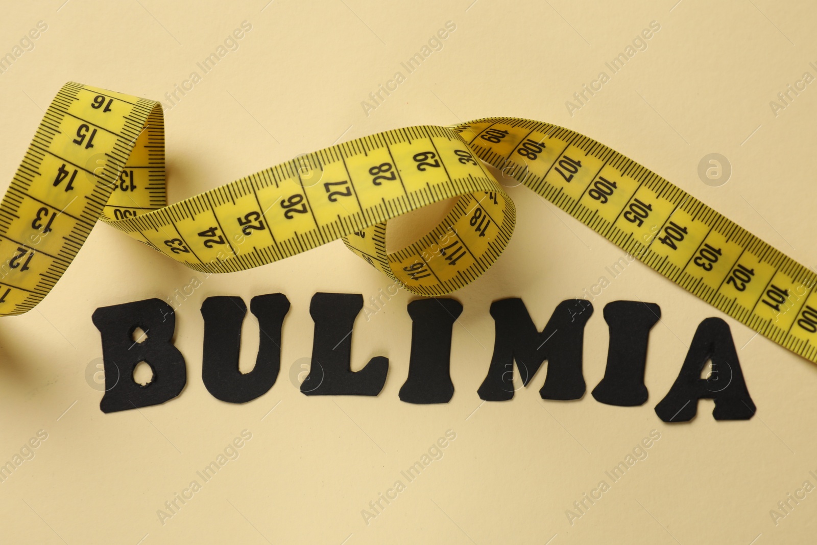 Photo of Word Bulimia and measuring tape on beige background, top view