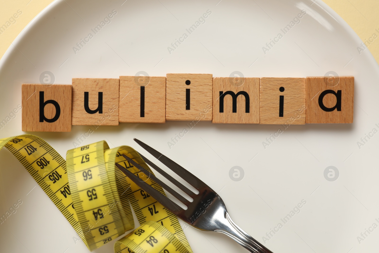 Photo of Plate with word Bulimia, fork and measuring tape on beige background, top view