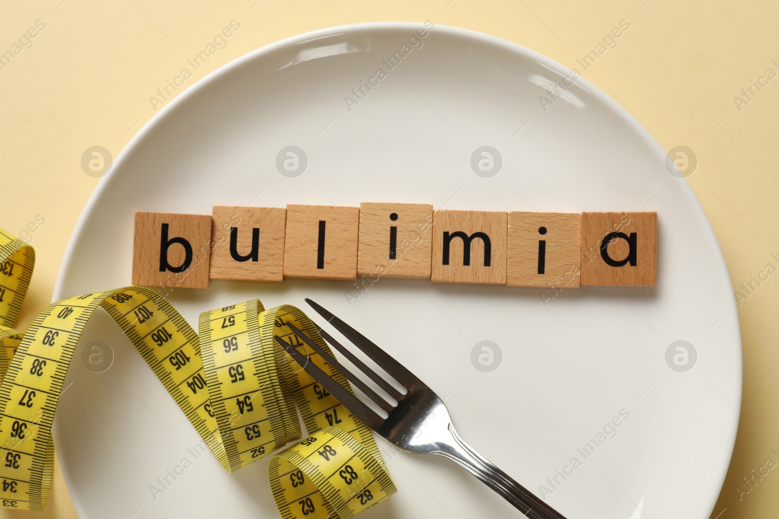 Photo of Plate with word Bulimia, fork and measuring tape on beige background, top view