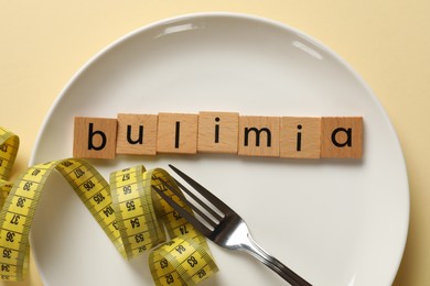 Photo of Plate with word Bulimia, fork and measuring tape on beige background, top view