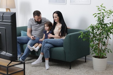 Photo of Cute little girl and her parents watching tv together at home