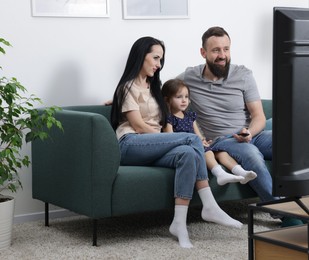 Photo of Cute little girl and her parents watching tv together at home