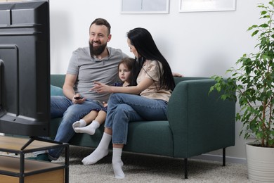 Photo of Cute little girl and her parents watching tv together at home