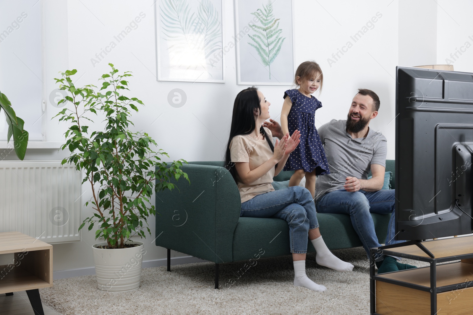 Photo of Cute little girl and her parents watching tv together at home