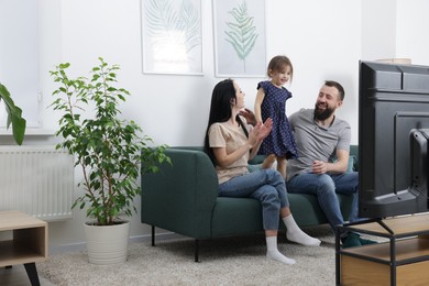 Photo of Cute little girl and her parents watching tv together at home