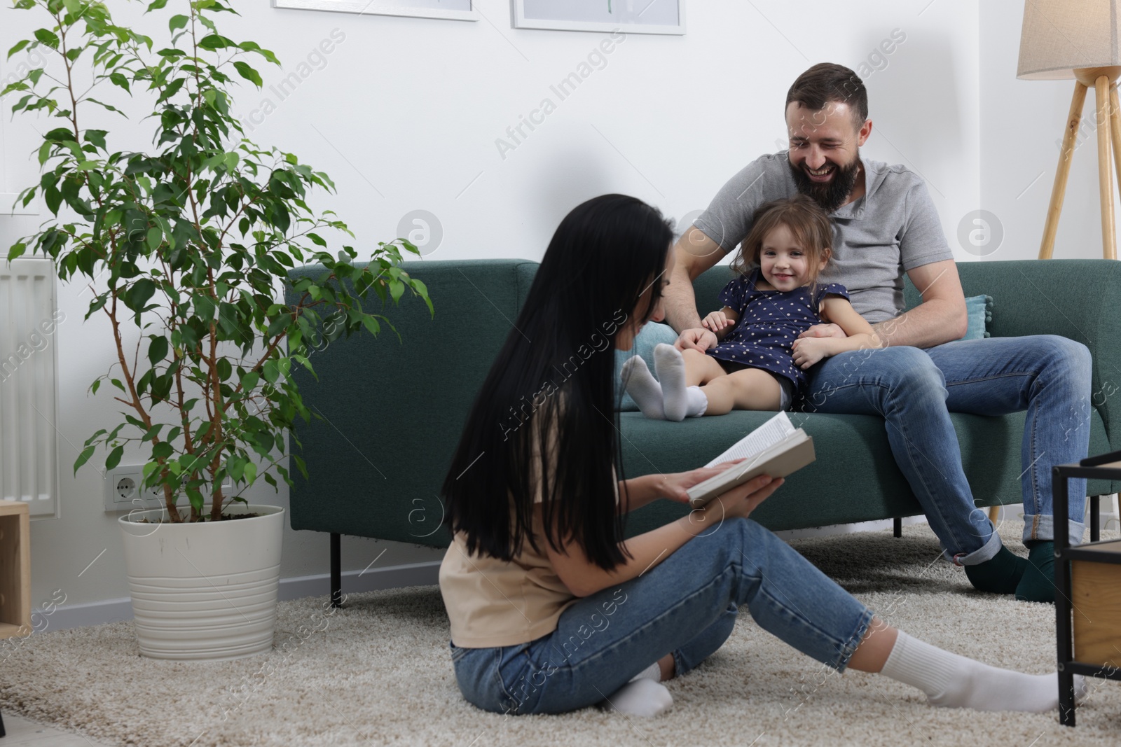 Photo of Cute little girl and her parents reading book together at home