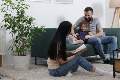 Photo of Cute little girl and her parents reading book together at home