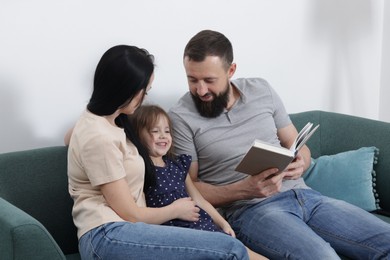 Photo of Cute little girl and her parents reading book together at home