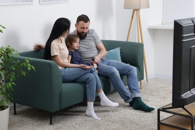 Photo of Cute little girl and her parents watching tv together at home